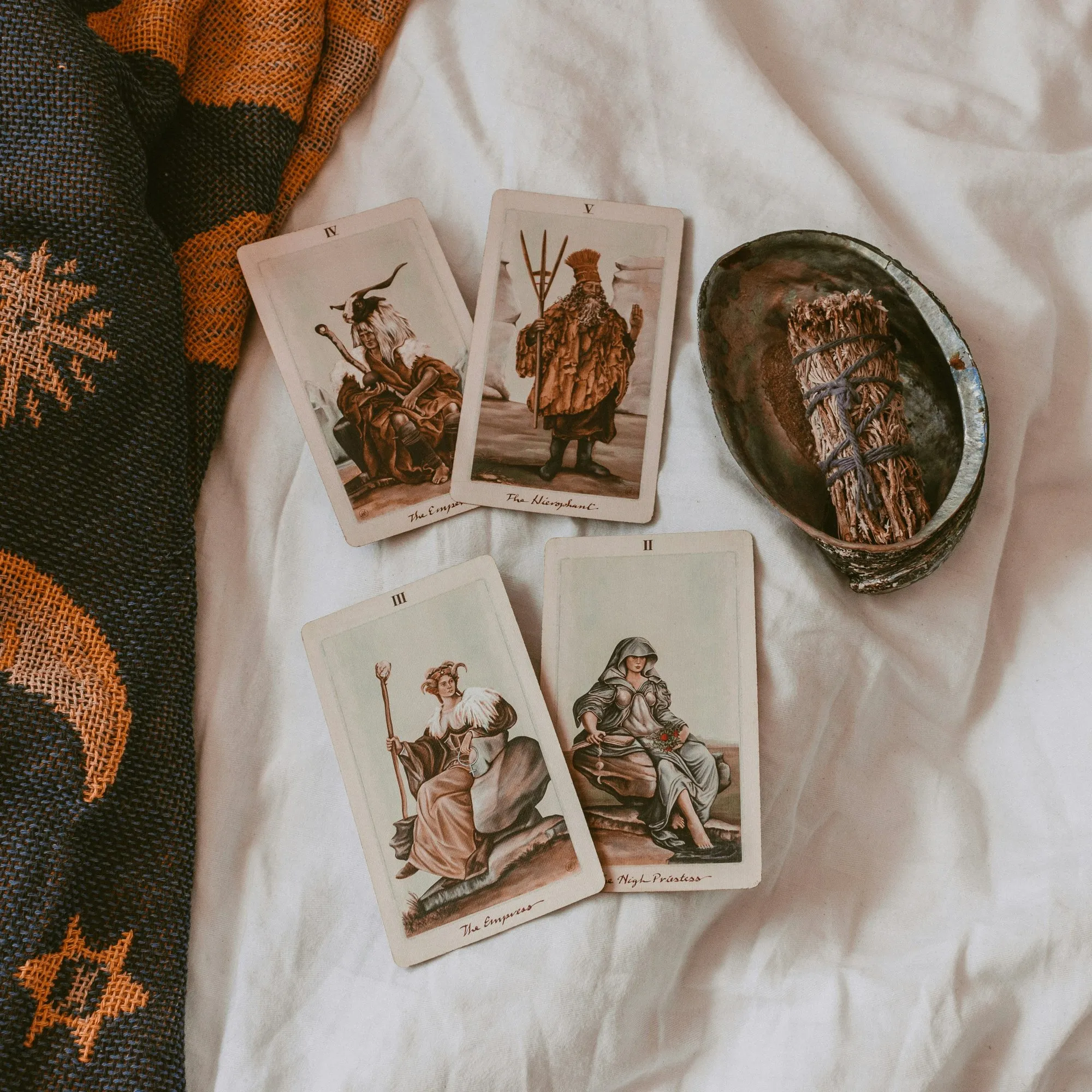 Quatre cartes de tarot posées sur un drap blanc, à côté d’un bâton de sauge dans une coquille