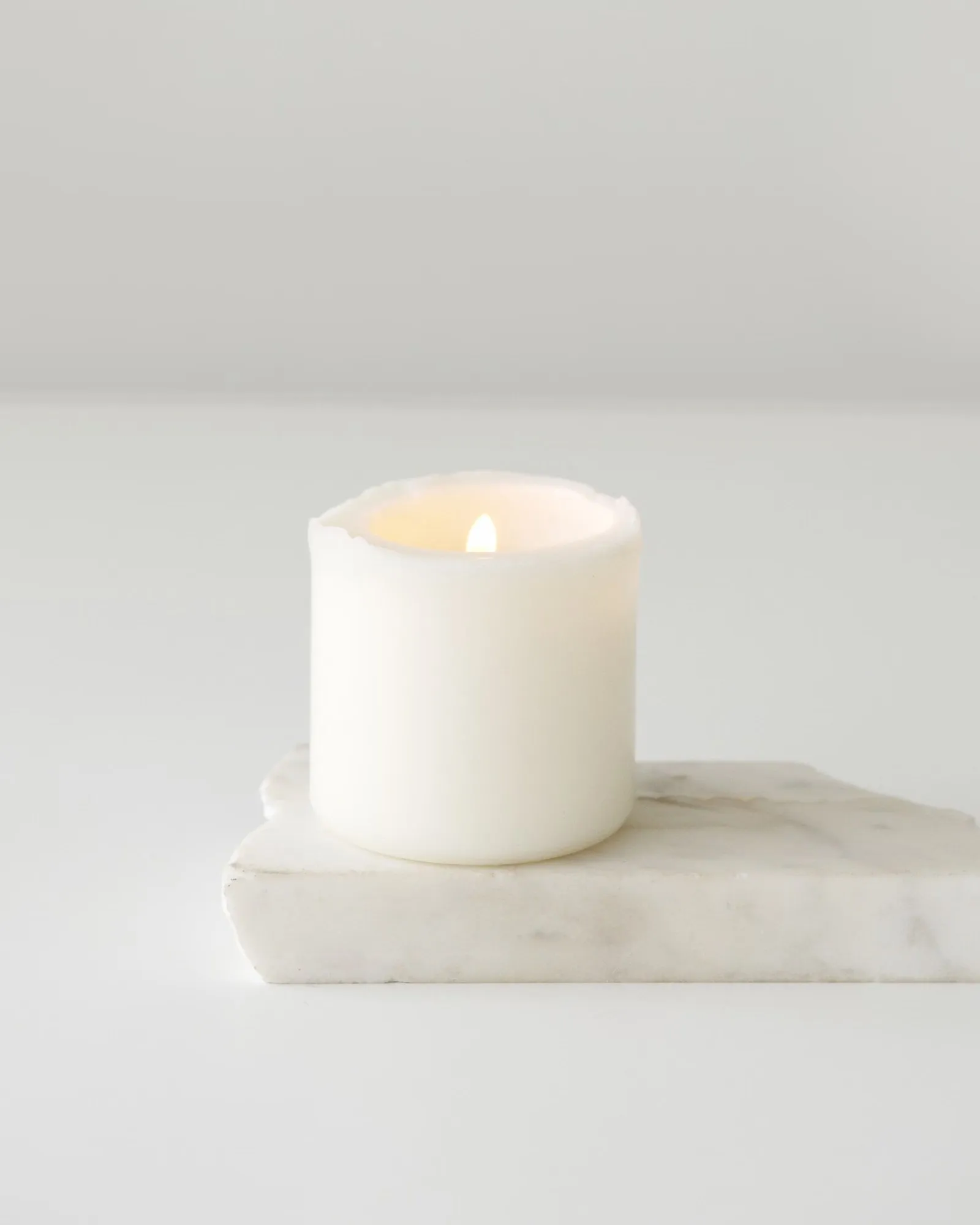 Bougie blanche allumée posée sur un socle de marbre