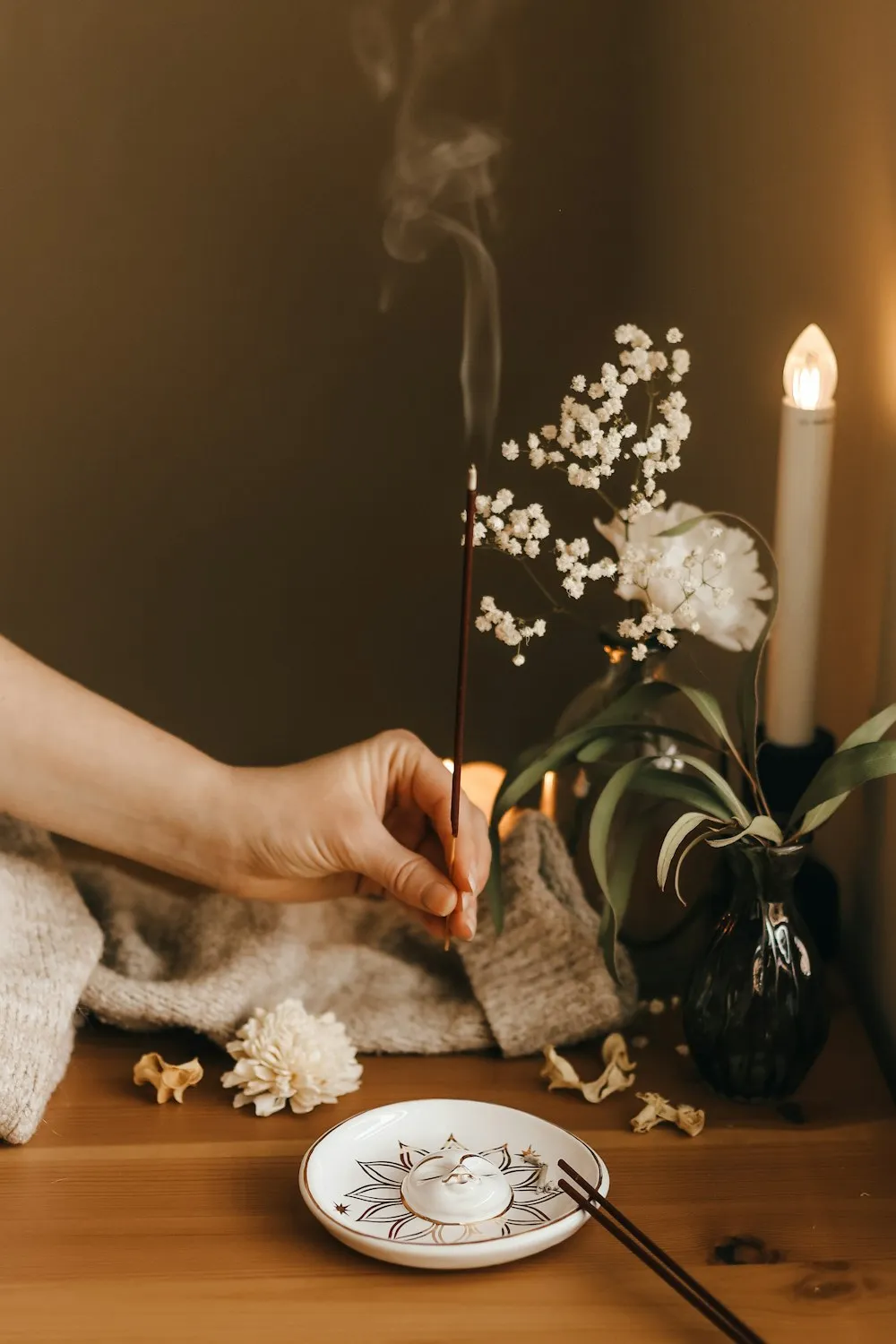Main déposant un bâton d’encens près d’une bougie et de fleurs blanches