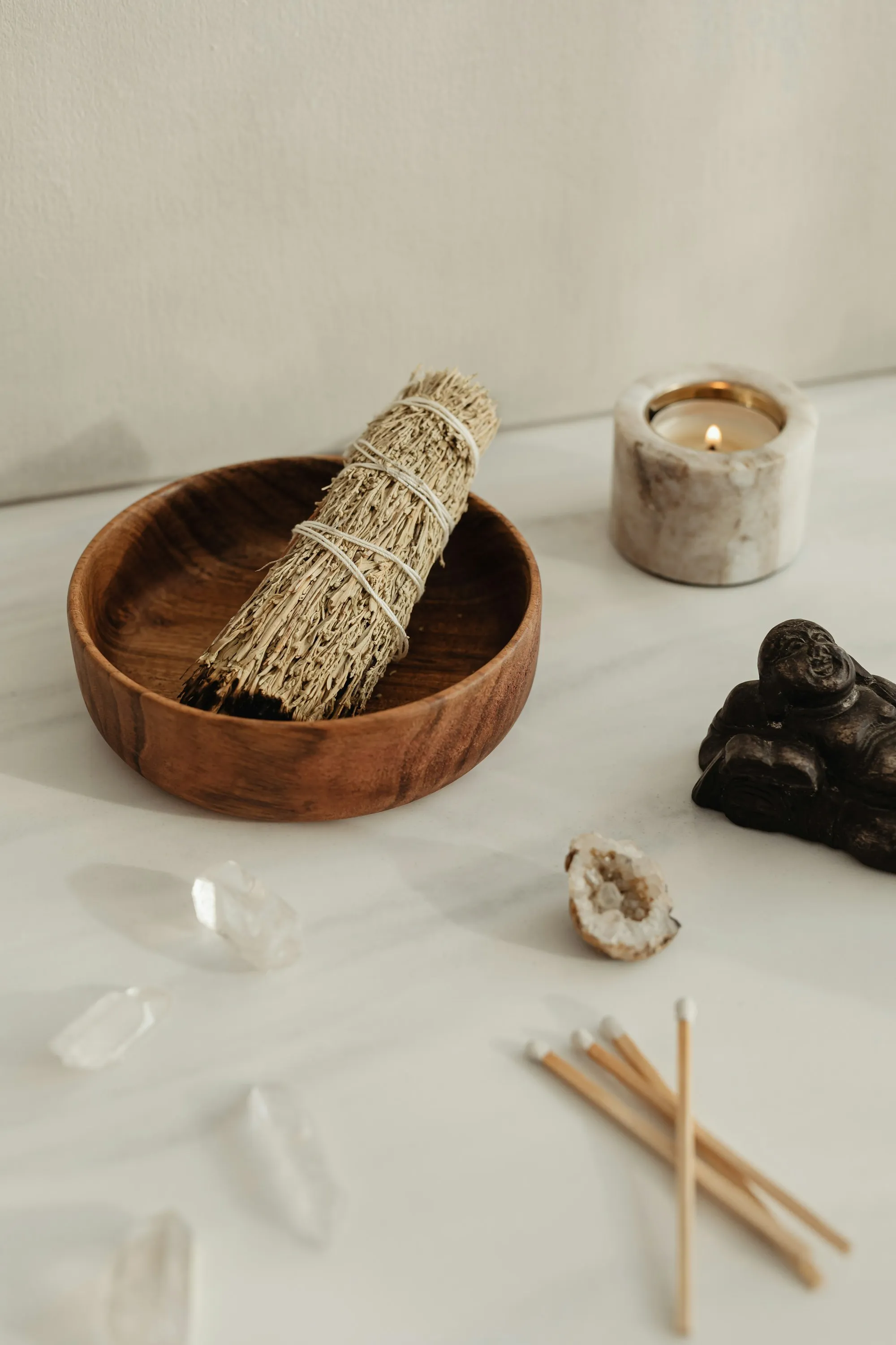 Bol de sauge, bougie allumée et cristaux posés sur une table claire, prêts pour une consultation